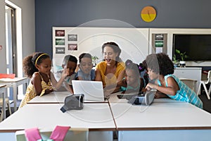 Young female caucasian teacher teaching laptop to african american elementary students in class