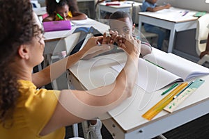 Young female caucasian teacher teaching sign language to african american elementary boy in class