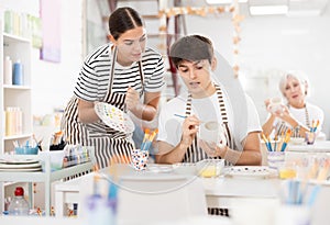 Young female ceramicist teaching guy to paint on ceramics in pottery studio