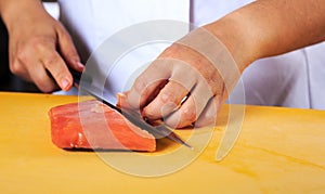 Young female chef coock dressed in white uniform cut salmon fish on the table in restaurant kitchen