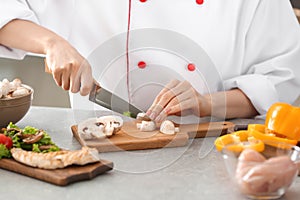 Young female chef cutting mushrooms in kitchen, closeup