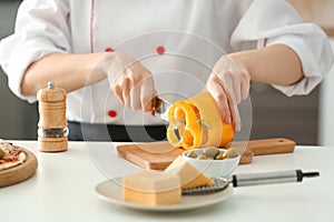 Young female chef cutting pepper in kitchen, closeup