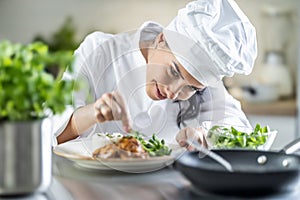 A young female chef finishes the meal with herbs in the restaurant kitchen