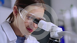young female chemical laboratorian is viewing into microscope, closeup of face