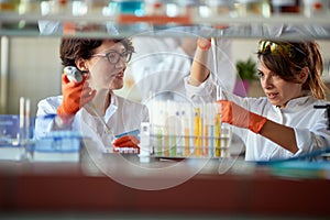 Young female chemistry students chatting while working with pipettes and test tubes in a laboratory. Science, chemistry, lab,