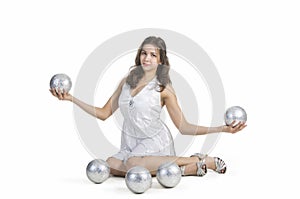 A young female circus performer, juggles silver balls.