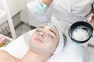 The young female client of cosmetic salon having a cleansing facial mask. The procedure of applying a peeling mask to the face