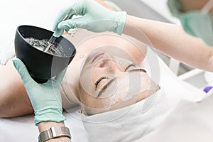 The young female client of cosmetic salon having a cleansing facial mask. The procedure of applying a peeling mask to the face