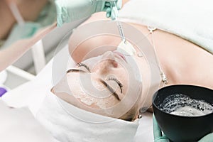 The young female client of cosmetic salon having a cleansing facial mask. The procedure of applying a peeling mask to the face