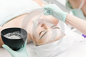 The young female client of cosmetic salon having a cleansing facial mask. The procedure of applying a peeling mask to the face