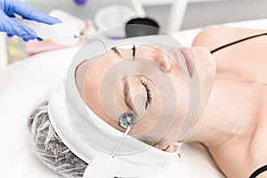 The young female client of cosmetic salon having microcurrent procedure on her face with special devices, close-up. Beautician
