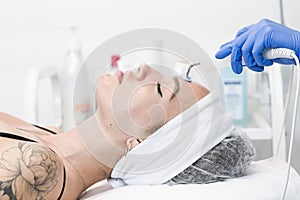 The young female client of cosmetic salon having microcurrent procedure on her face with special devices, close-up. Beautician