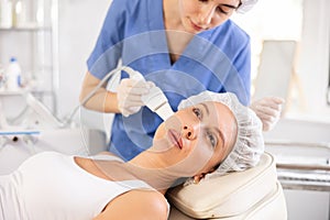 Young female client experiencing facial skin peeling using ultrasonic scrubber