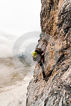 Young female climber on a vertical and exposed rock face climbing a Via Ferrata