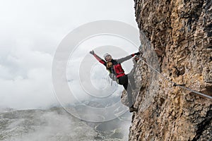 Young female climber on a vertical and exposed rock face climbing a Via Ferrata