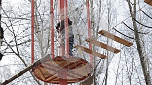 Young female climber walks by pendant log bridge on high ropes course in extreme park