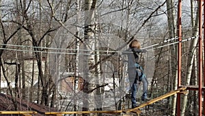 Young female climber walks by pendant log bridge on high ropes course in extreme park