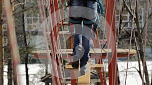 Young female climber walks by pendant log bridge on high ropes course in extreme park