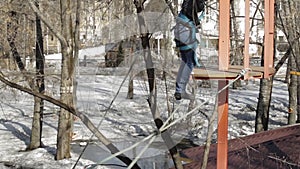 Young female climber walks by pendant log bridge on high ropes course in extreme park