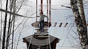 Young female climber walks by pendant log bridge on high ropes course in extreme park