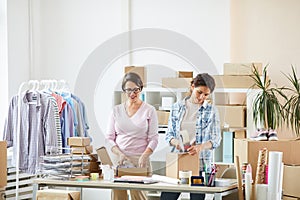 Young female colleagues standing by desk while making parcels for clients