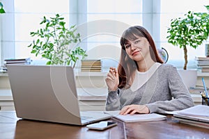 Young female college student studying at home using laptop, looking at camera