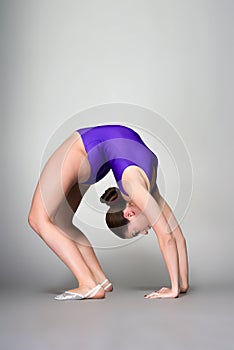 Young female contortionist in purple leotard on dark background