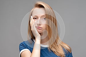 Young female covers face, feels fatigue, dressed in blue t shirt, has sleepy expression. Weariness and people