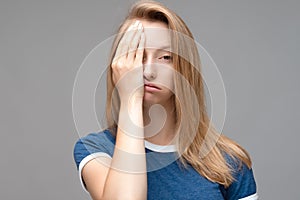 Young female covers face, feels fatigue, needs good rest, dressed in blue t shirt. Weariness concept