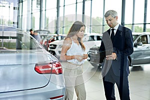 Young female customer asking mature sales manager to help in car dealership.