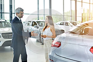 Young female customer asking mature sales manager to help in car dealership.