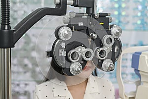 Young female customer being examined visual test using Bifocal Optometry eyesight measurement device by ophthalmologist in optical photo