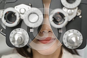 Young female customer being examined visual test using Bifocal Optometry eyesight measurement device by ophthalmologist in optical photo