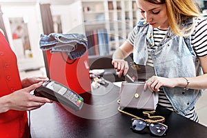 Young female customer standing at cash desk paying with credit card in clothing shop