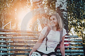Young female cyclist resting on an old wooden bench in the park. Sunbeams