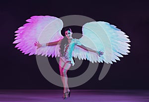 Young female dancer with angel`s wings in neon light on black background