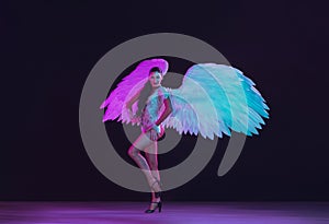 Young female dancer with angel`s wings in neon light on black background
