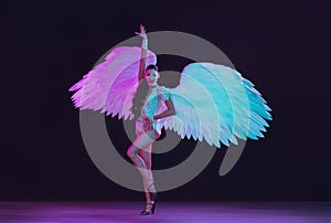 Young female dancer with angel`s wings in neon light on black background