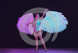 Young female dancer with angel`s wings in neon light on black background