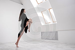 A young female dancer in a black dress is stretching by the window. White Hall, the working class, yoga asanas.