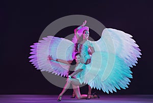 Young female dancers with angel`s wings in neon light on black background