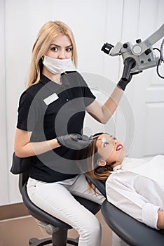 Young female dentist with beautiful woman patient during treatment with microscope in dental office. Dentistry