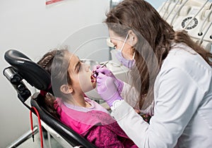 Young female dentist is checking up patient girl teeth at dental office