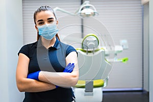 Young female dentist doctor in mask stands in the office with his arms crossed.