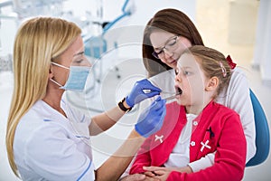 Young female dentist looks at girls teeth