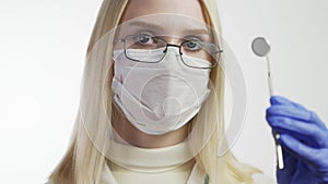 Young Female Dentist in Mask Approaches With Tools, Holding a Mouth Mirror and Dentist`s Hook