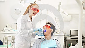 Young female dentist in UV protective glasses using dental curing light during composite filling