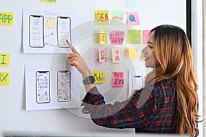 Female designer planning mobile app development prototype wireframe design on whiteboard.
