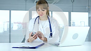 Young female doctor browsing online on phone in hospital