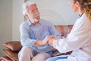 Young female doctor checking and helping senior man at his home. Doctor helping senior patient and giving care, sitting of sofa.